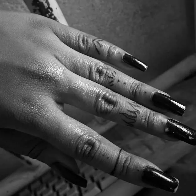 Mão com unhas pretas e pequenos ornamentos tatuados em blackwork sobre os dedos