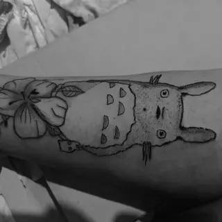 Totoro com folha na cabeça, tatuagem no antebraço